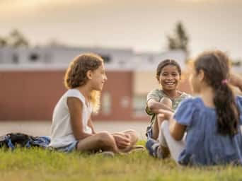 Smiling children sitting on a field, engaged in a funny conversation